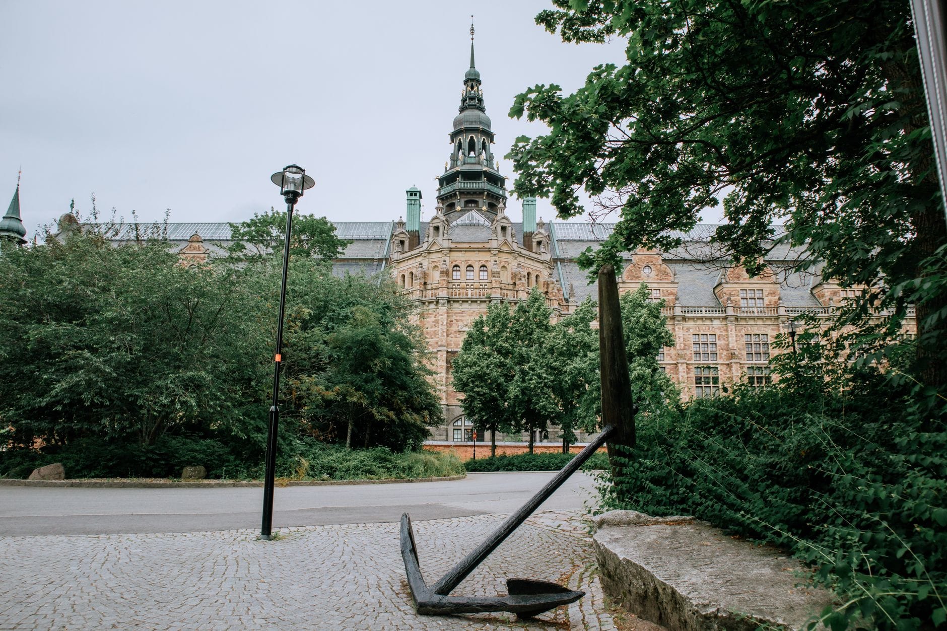 ด้านหน้าอันยิ่งใหญ่ของ Nordiska Museet ในสตอกโฮล์ม ล้อมรอบด้วยต้นไม้เขียวชอุ่มและประติมากรรมสมอเรือขนาดใหญ่ด้านหน้า