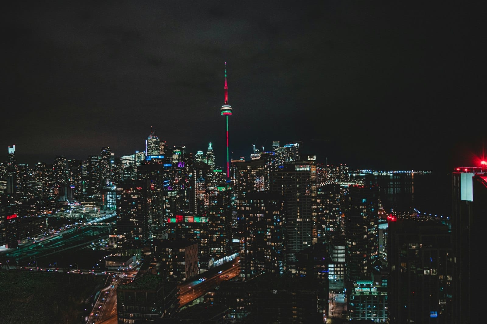 O skyline de Toronto à noite com a CN Tower iluminada no centro, cercada por arranha-céus acesos contra um céu escuro.