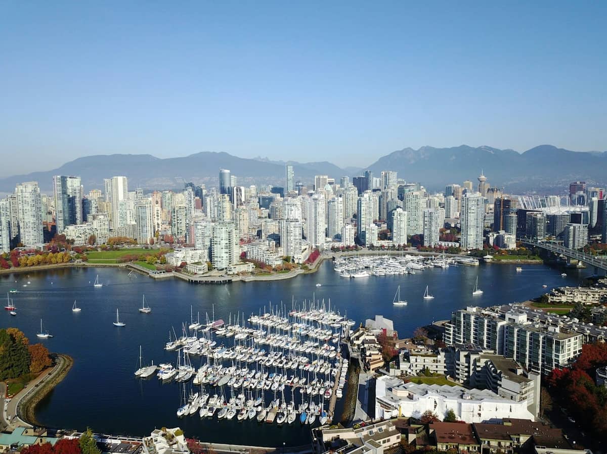 Luftaufnahme der Vancouver-Marina mit Yachten, moderner Stadtsilhouette, Bergen im Hintergrund und Wasser im Vordergrund an einem klaren Tag.
