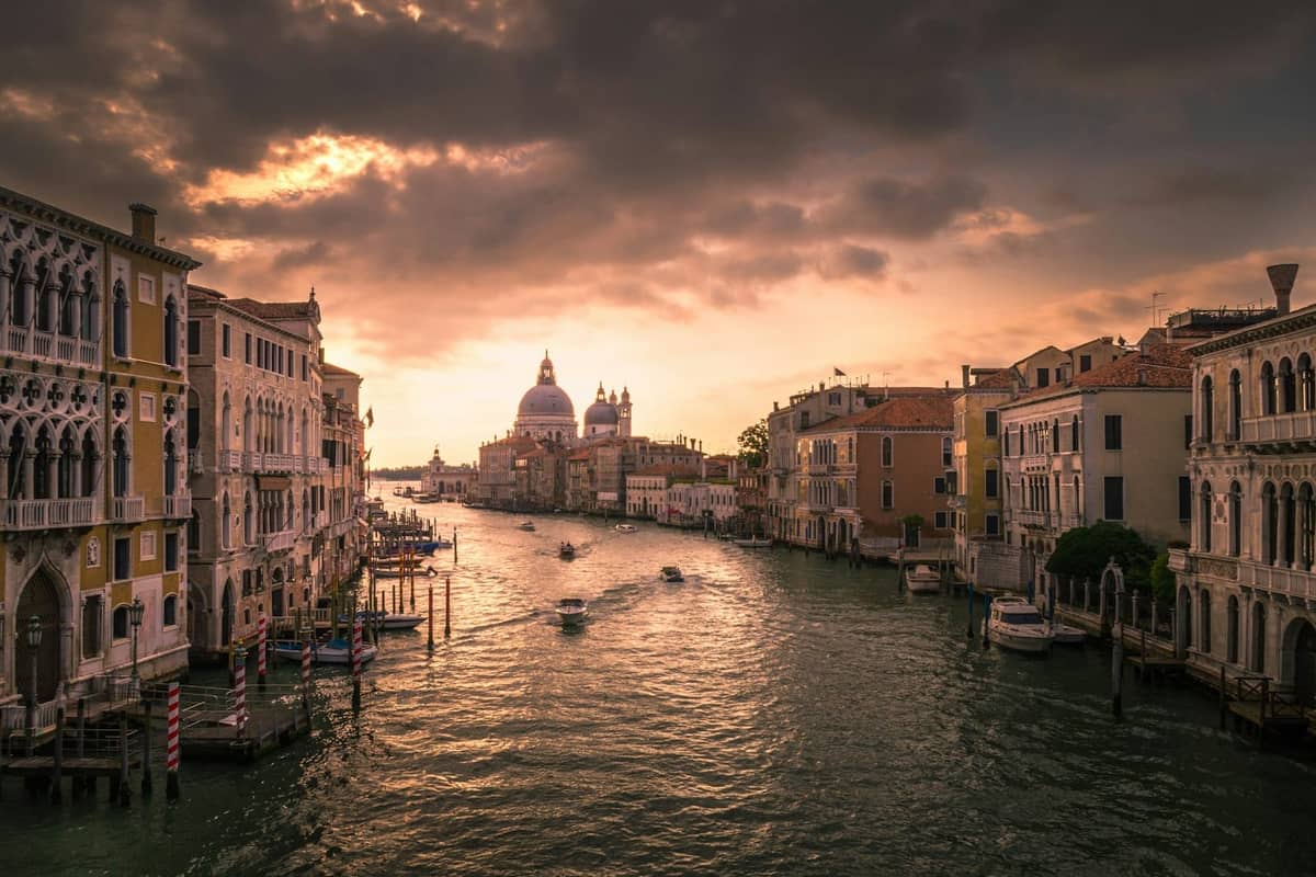 Dramatischer Sonnenuntergang über dem Canal Grande in Venedig mit den Kuppeln von Santa Maria della Salute, historischen Palazzi und Booten auf dem Wasser.