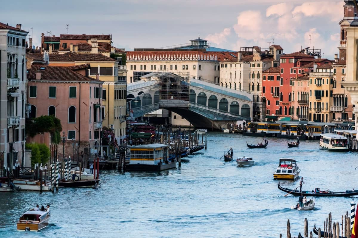 Weitblick den Canal Grande in Venedig hinunter mit der Rialtobrücke, historischen Palästen auf beiden Seiten sowie Booten und Gondeln auf dem Wasser.