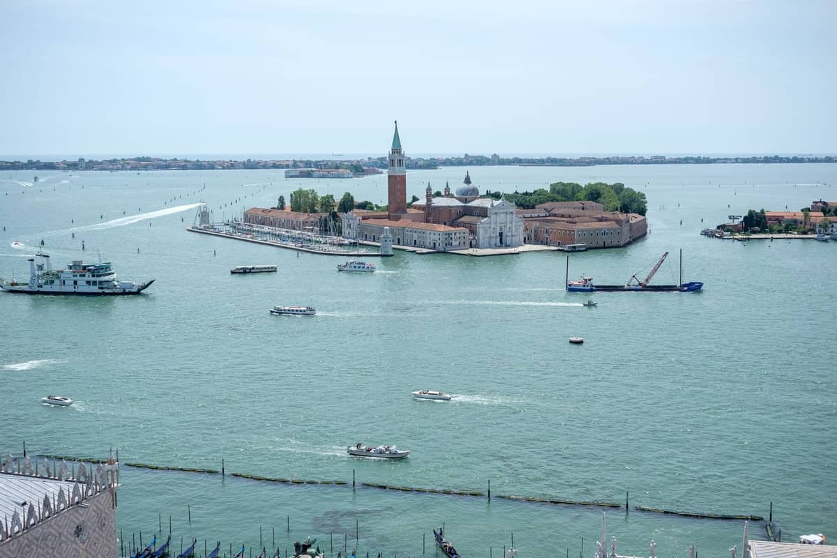 Weitwinkelansicht der Insel San Giorgio Maggiore mit ihrer Kirche, dem Glockenturm und Booten in der venezianischen Lagune unter bewölktem Himmel.