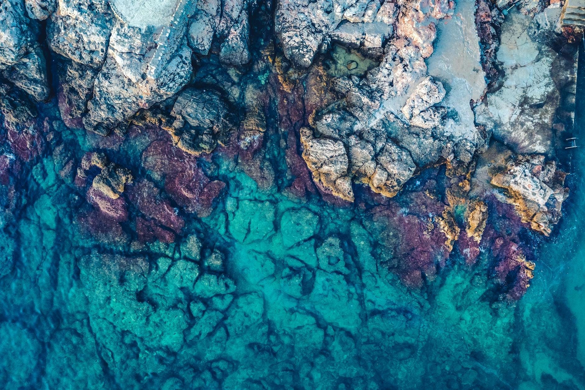 Vista aérea del mar turquesa contra escarpados acantilados de piedra caliza, con aguas cristalinas y texturas rocosas que evocan una cueva costera escondida y tranquila.