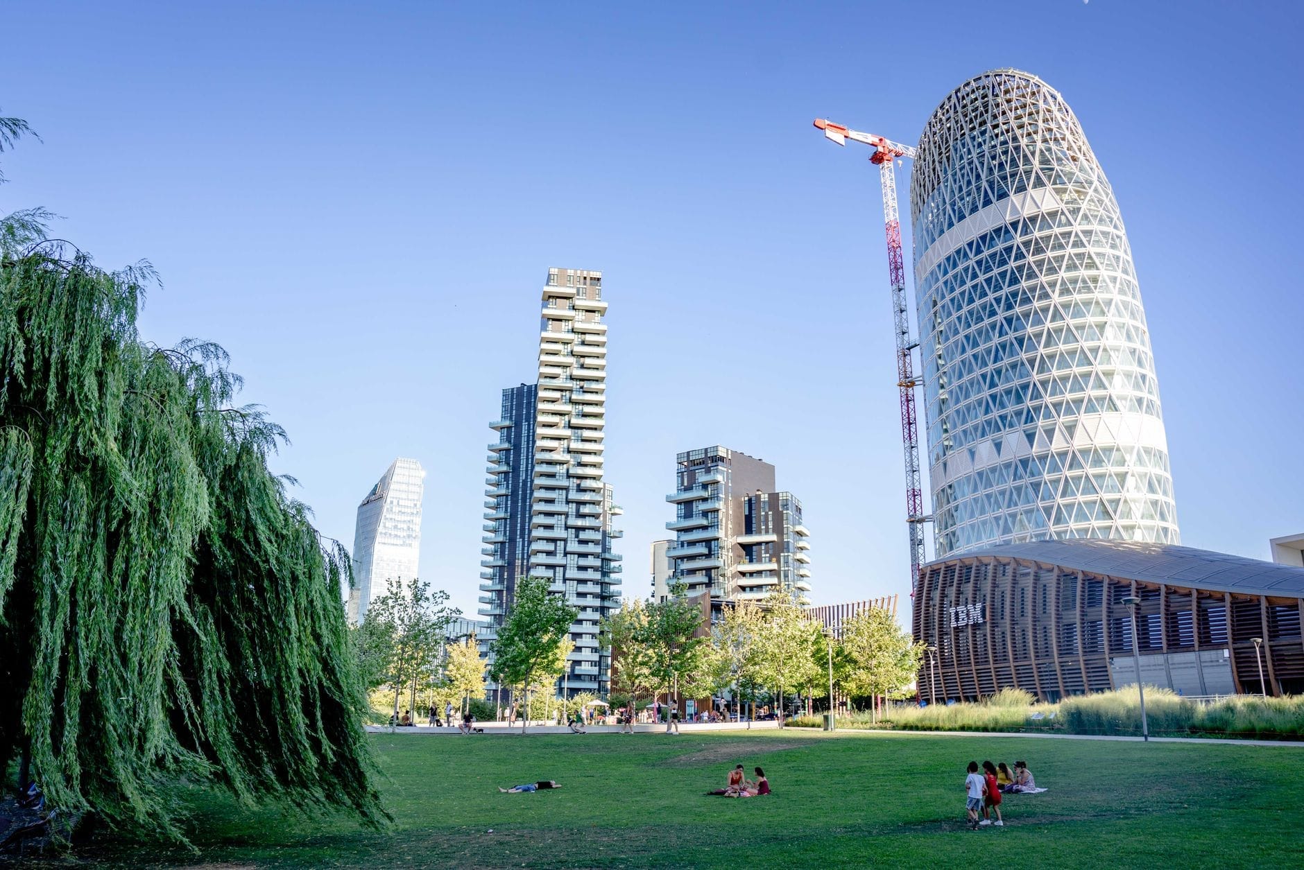Un parco rigoglioso incorniciato da grattacieli moderni, con persone che si rilassano sull'erba: la contemporanea Biblioteca degli Alberi Milano nel quartiere Porta Nuova.