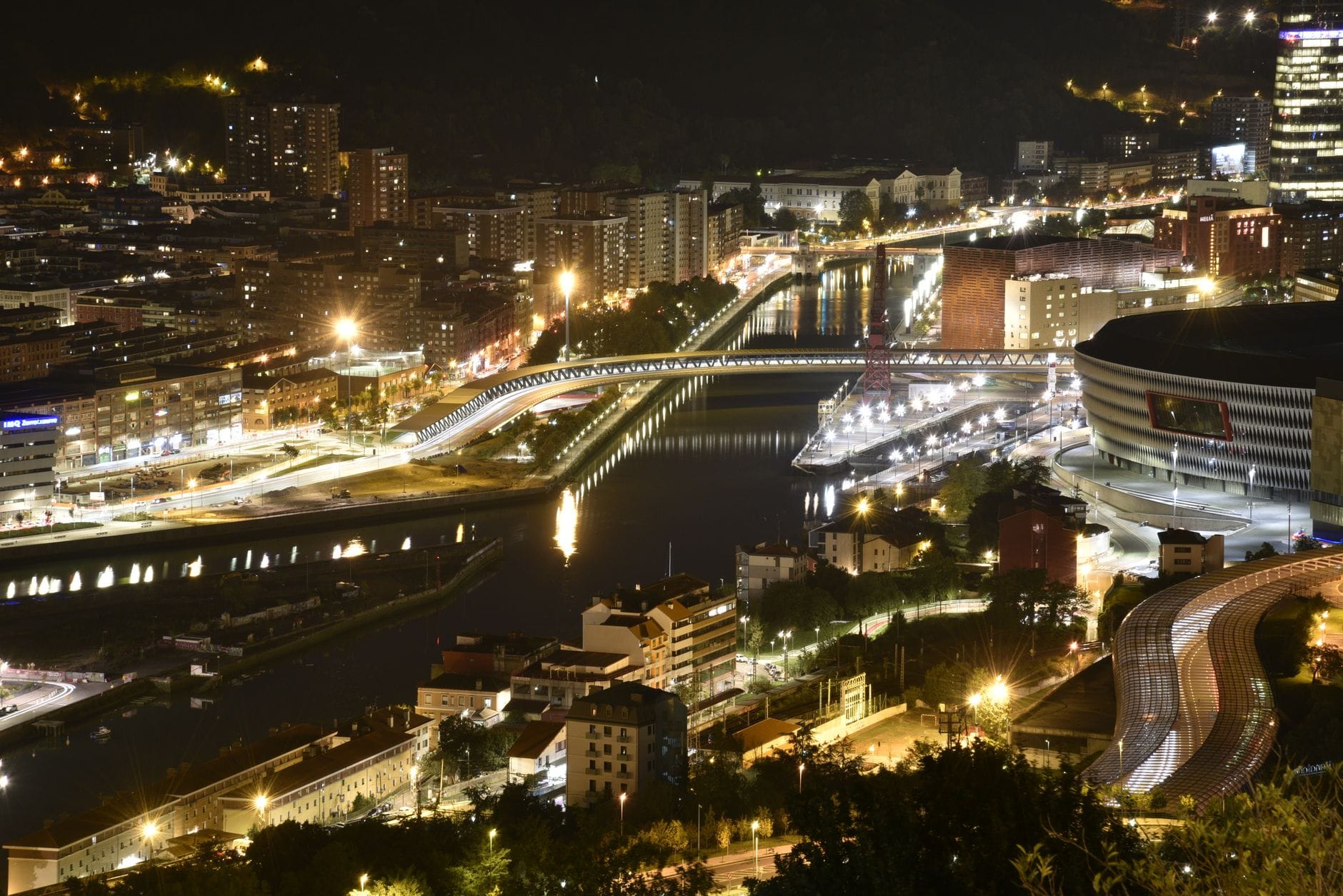 A nighttime aerial view of Bilbao's city center and river brightly lit for festivities, capturing the excitement and atmosphere of a major festival event.