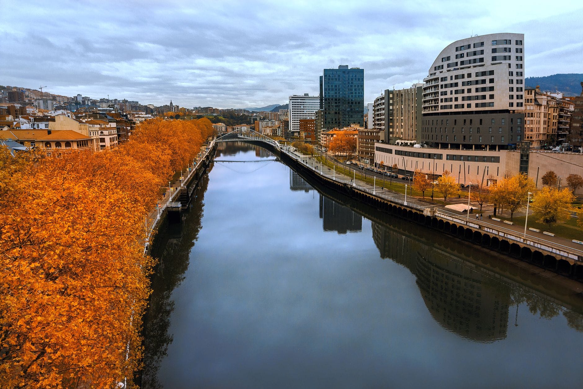 Rzeka przecina centrum Bilbao, otoczona jesiennymi drzewami i nowoczesnymi budynkami, ukazując zwarty i przyjazny pieszym rdzeń miasta.