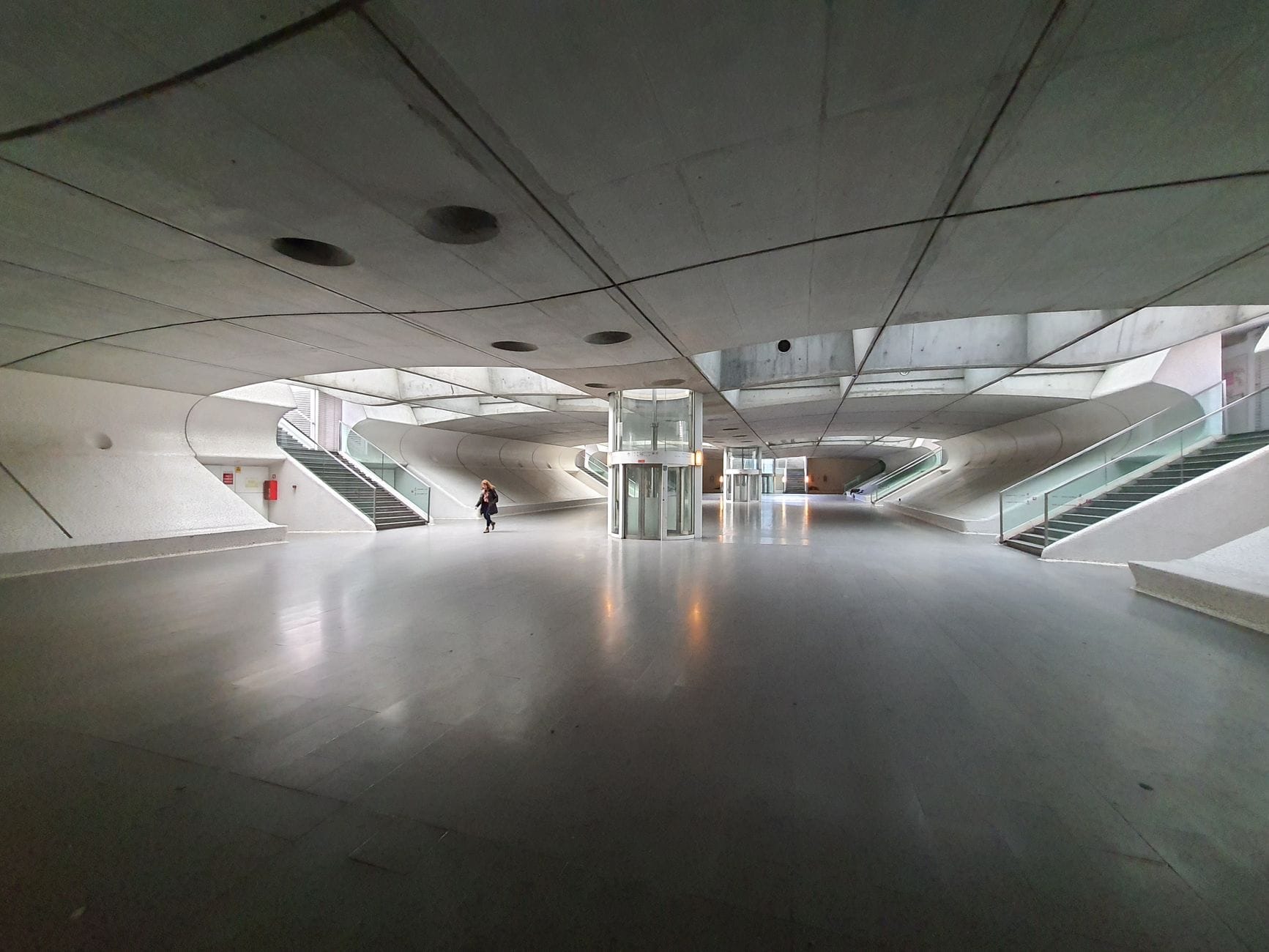 Bilbao'da kavisli beton duvarlara, cam asansörlere ve merdivenlere sahip modern bir kapalı kamusal alanın geniş görünümü, yağmurdan korunmak için uygun.