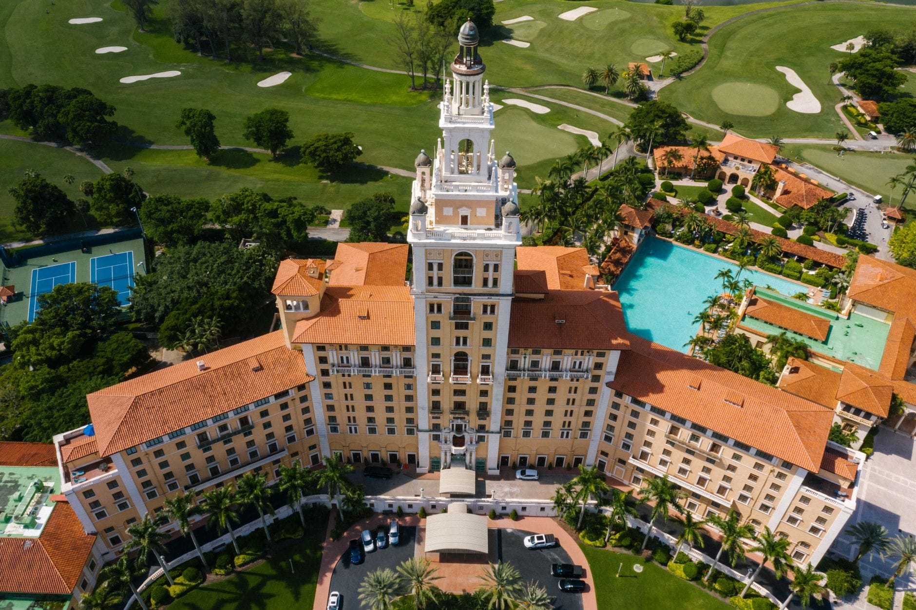 Vista aerea del Biltmore Hotel di Coral Gables con la sua iconica torre, i tetti rossi, i giardini lussureggianti e il campo da golf circostante in una giornata di sole.