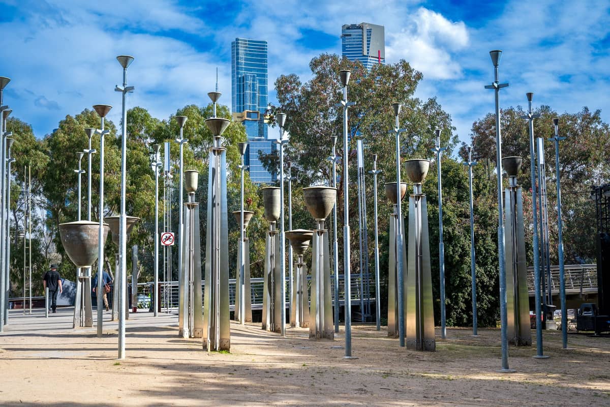 El parque Birrarung Marr en Melbourne con la instalación Federation Bells, árboles y rascacielos de la ciudad al fondo en un día soleado.