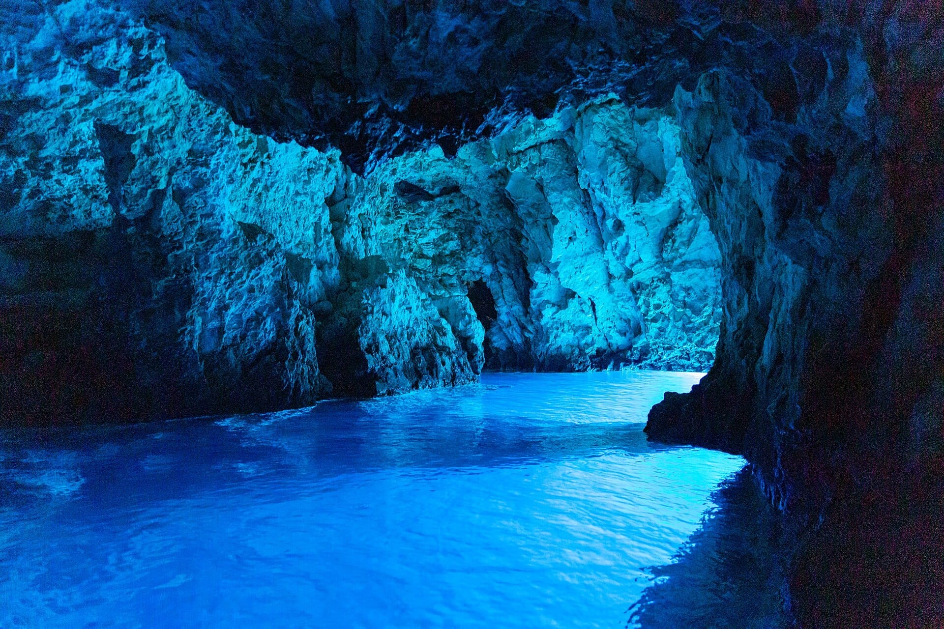 แสงอาทิตย์สะท้อนบนน้ำสีฟ้าคราม ภายใน Blue Cave ที่เป็นโขดหินบนเกาะ Biševo ส่องสว่างผนังหินด้วยแสงสีน้ำเงินอันสดใส