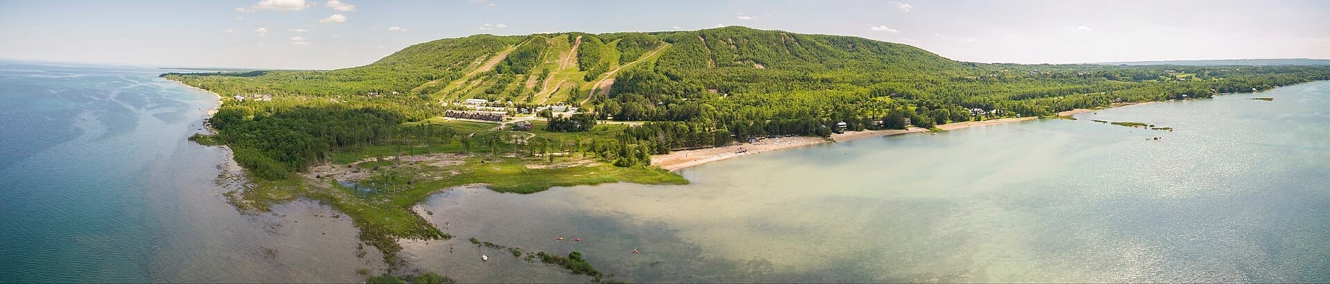 มุมมองทางอากาศของ Blue Mountain และ Collingwood พร้อมลานสกี ป่าสีเขียวชอุ่ม แนวชายฝั่ง และ Georgian Bay ที่แวววาวในวันที่แดดจ้า