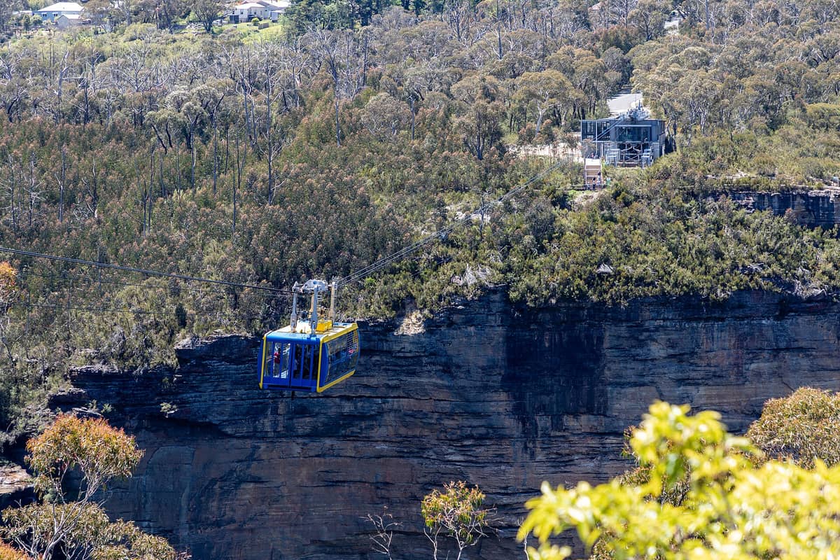 Die verglaste Scenic Skyway-Seilbahn fährt über eine tiefe Schlucht in den Blue Mountains mit bewaldeten Klippen und der im Sonnenlicht sichtbaren Oberstation.