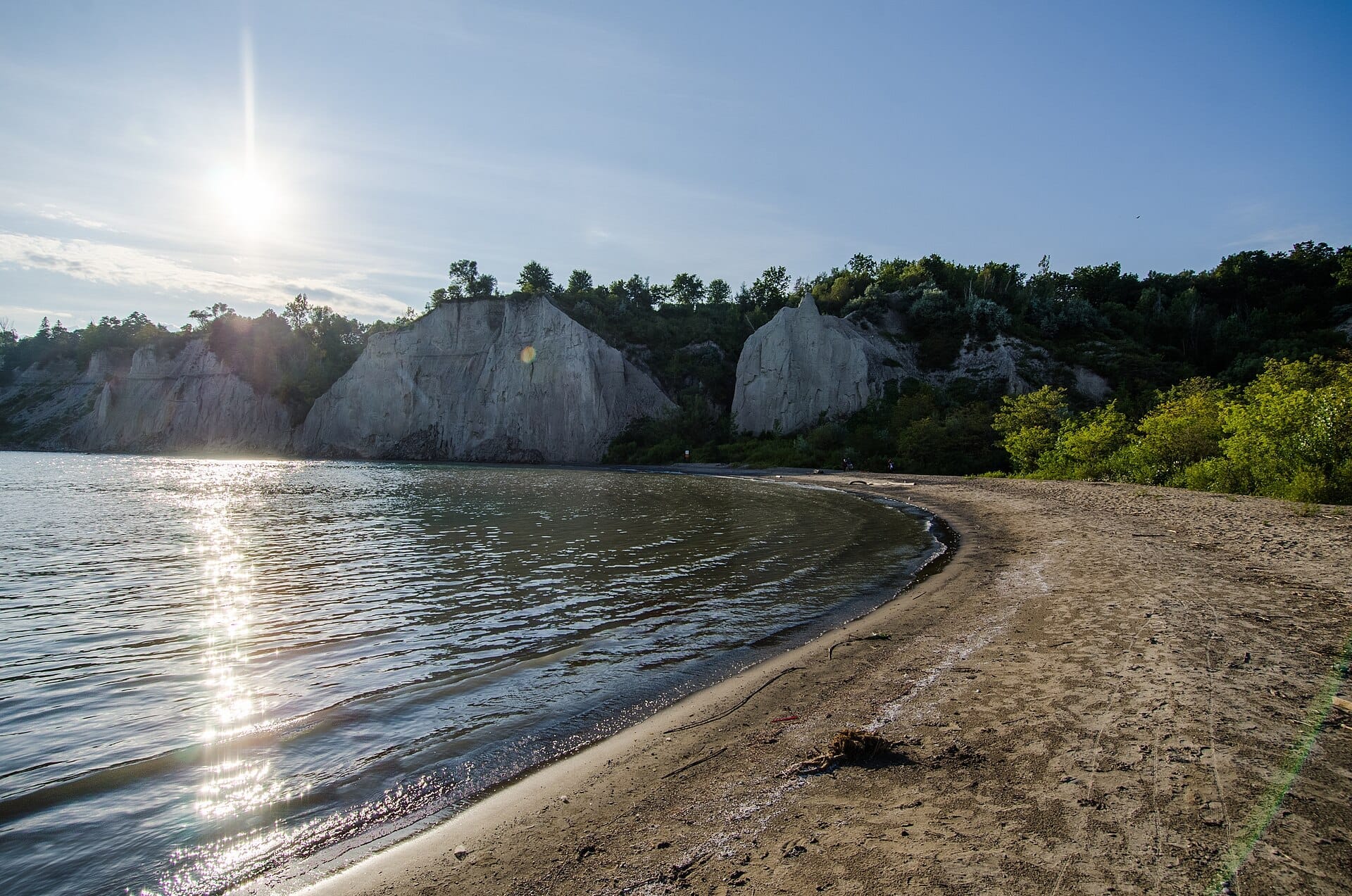 ชายฝั่งทรายที่ Bluffer's Park and Beach พร้อมน้ำทะเลสาบที่สงบนิ่งและ Scarborough Bluffs ที่สูงตระหง่านภายใต้ท้องฟ้าแจ่มใสและแดดจัด