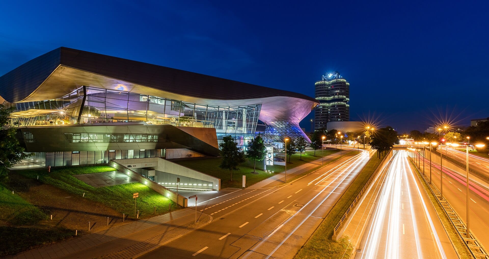 BMW Welt มิวนิกยามค่ำ สถาปัตยกรรมล้ำสมัยไฟสีม่วงเหลือง และตึกสำนักงานใหญ่ BMW ทอดฉากหลัง