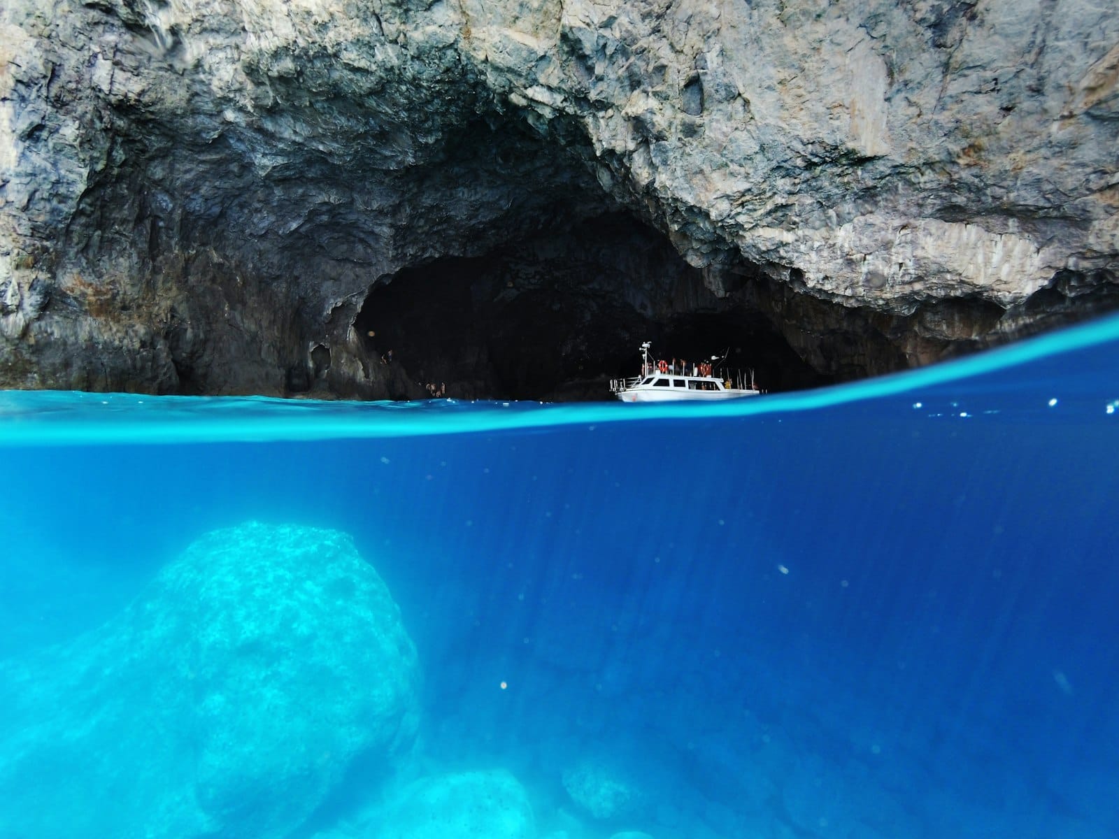 Um barco flutua na entrada da Gruta Azul com água turquesa brilhante abaixo e paredes rochosas acima, capturando a emoção dos passeios pelas ilhas saindo de Split.