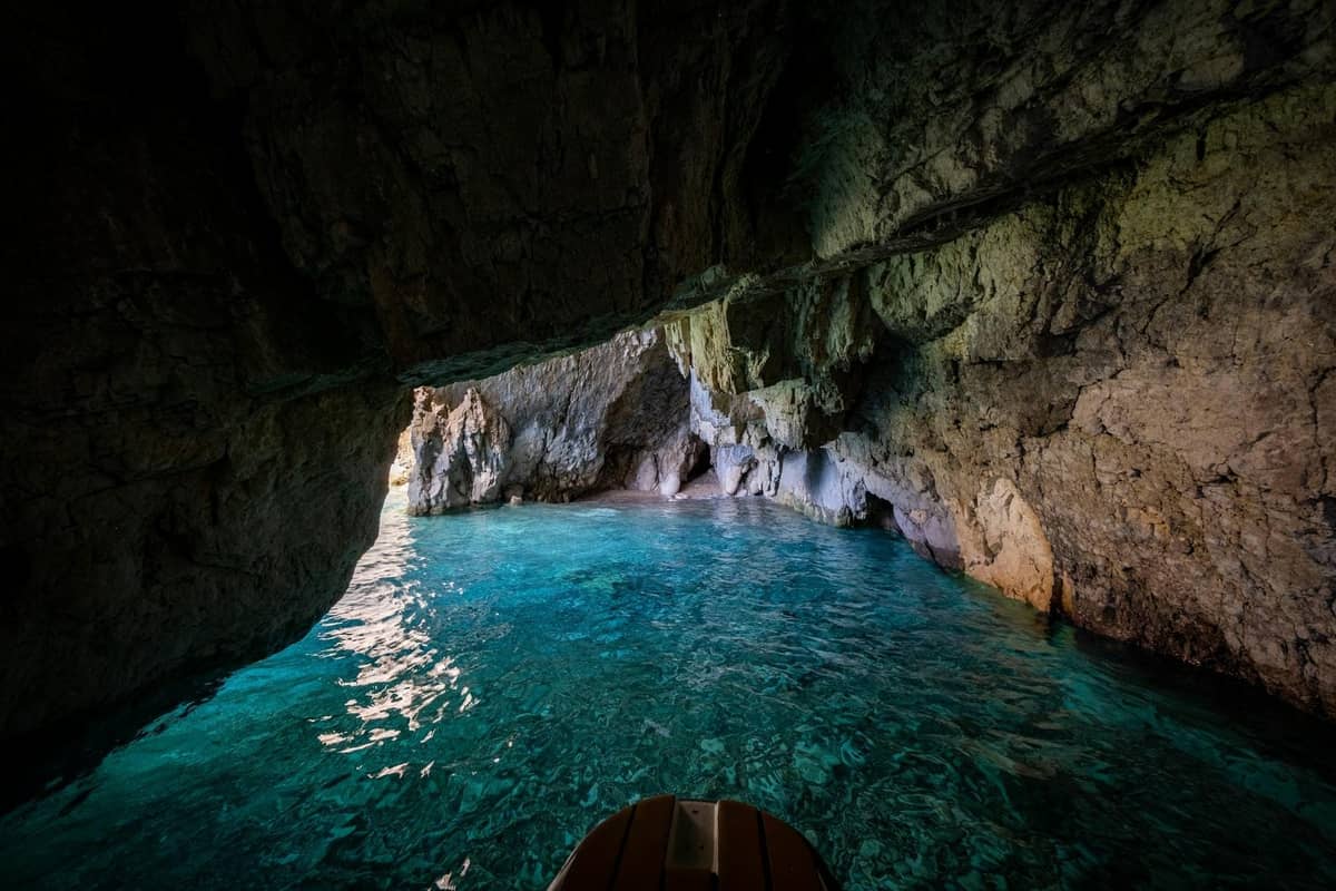 Blick aus dem Inneren einer Meereshöhle mit leuchtend türkisblauem Wasser und natürlichen Felswänden, mit Blick auf den Eingang und das sonnenbeschienene Meer.