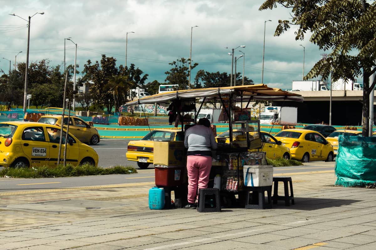 Line of yellow taxis waiting near a curb outside with street vendor, typical scene near Bogotá El Dorado Airport