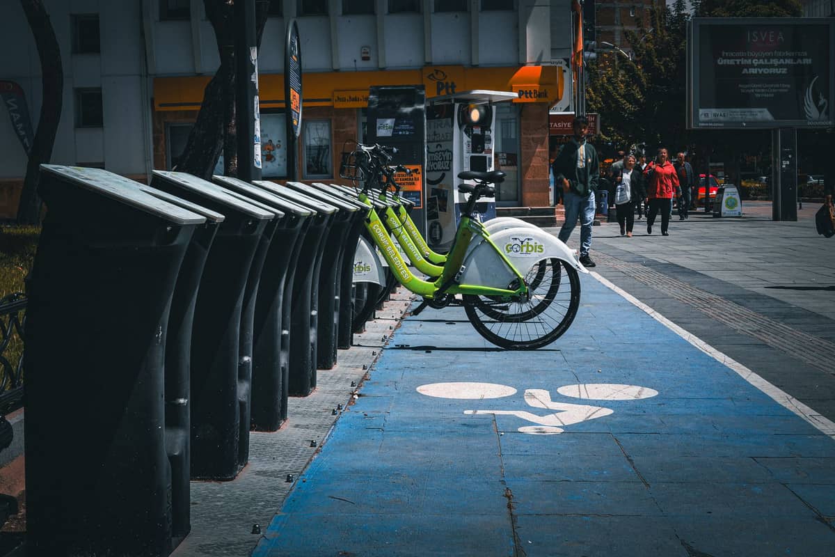 Bogotá city bike share station with green bikes on a blue cycle lane, buildings and people nearby on a cloudy day.