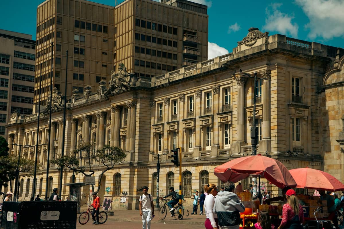 People walking, cycling, and gathering in front of a historic building in downtown Bogotá on a sunny day.