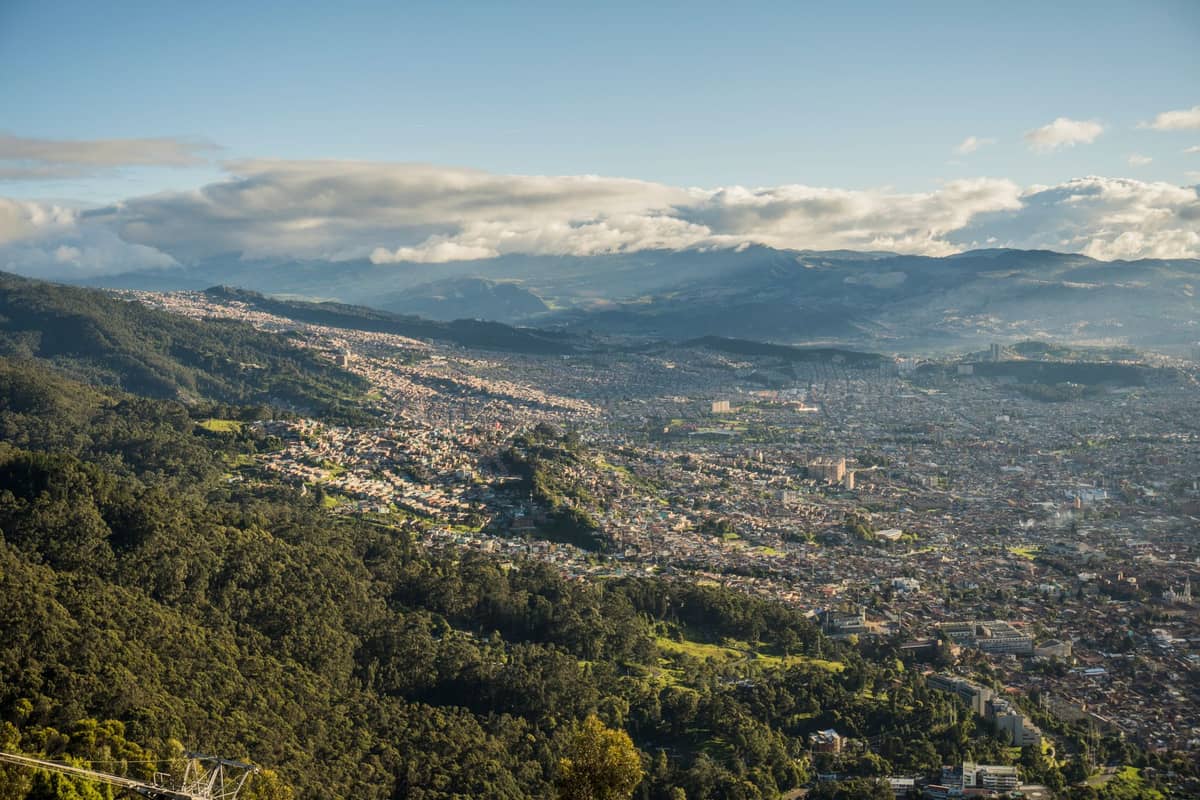 Wide landscape view of Bogotá showing the urban sprawl climbing into the Andean mountains under partly cloudy skies.