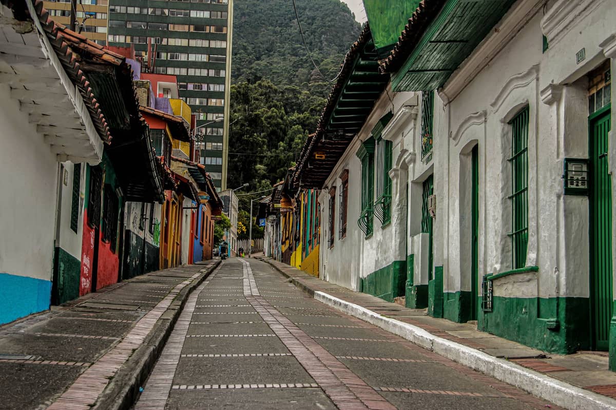 Narrow pedestrian street in Bogotá with colorful historic houses on each side and tall buildings in the background.