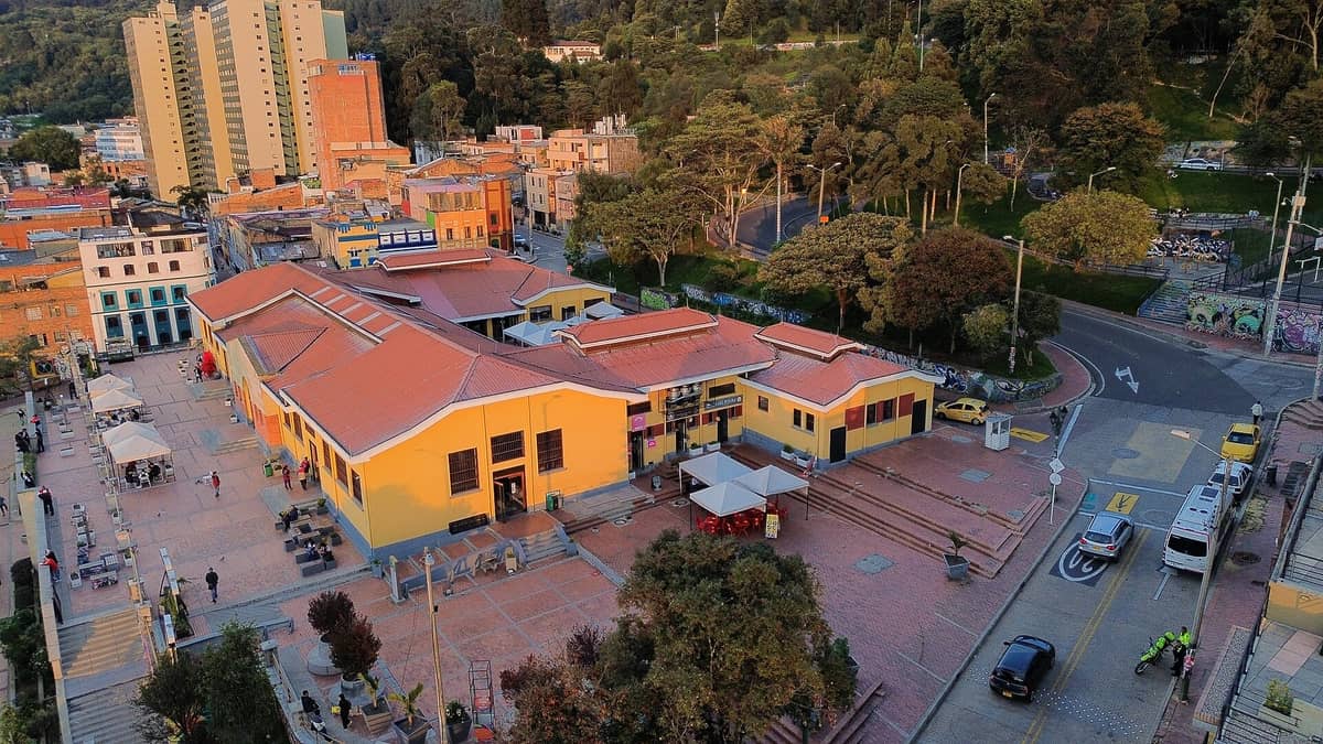 Aerial view of Bogotá’s historic La Candelaria district showing a well-known market building and surrounding streets with shops and colorful buildings.