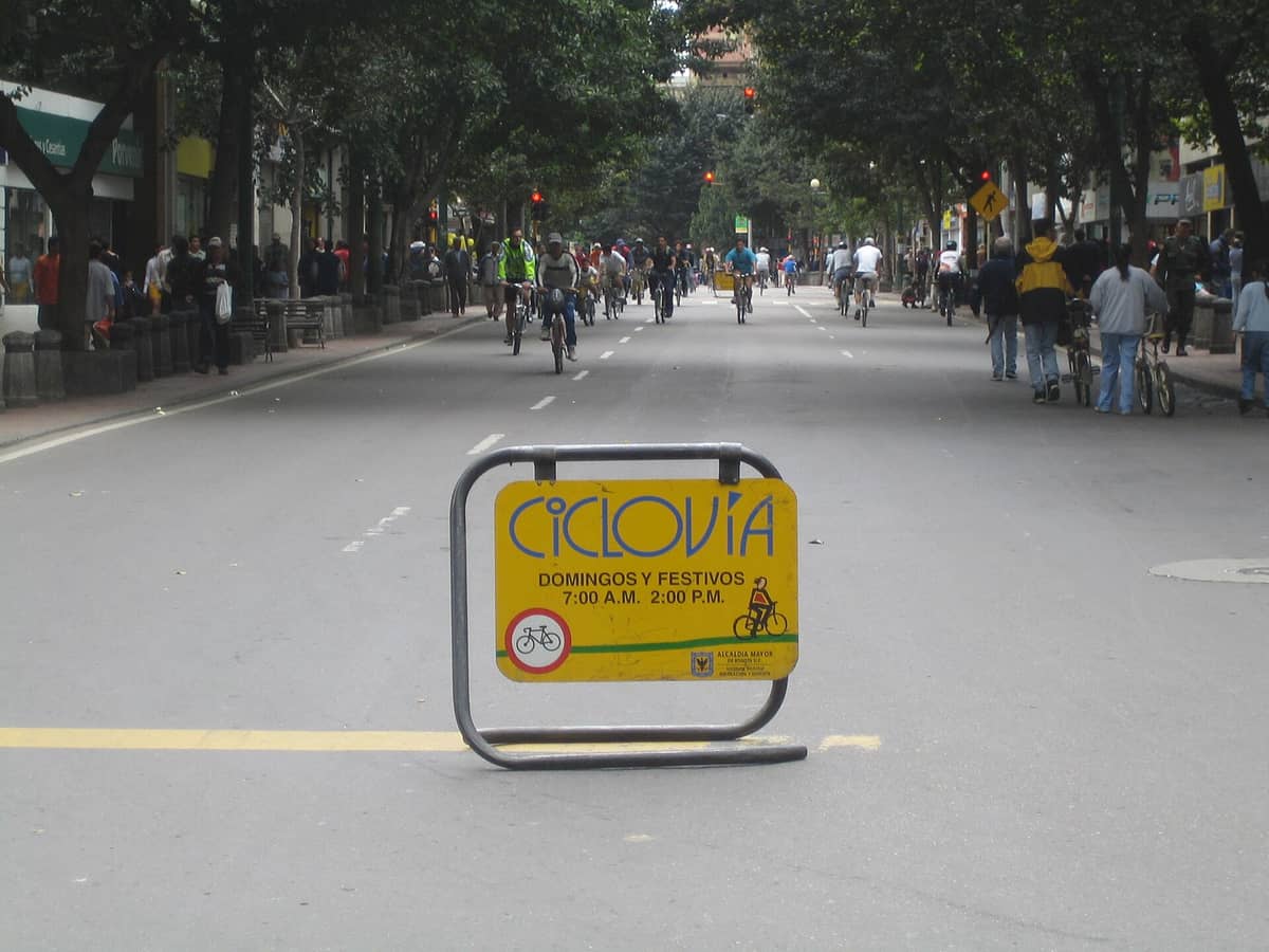 Street in Bogotá closed to cars for Ciclovía, with cyclists, pedestrians, and a large sign marking the Sunday event.