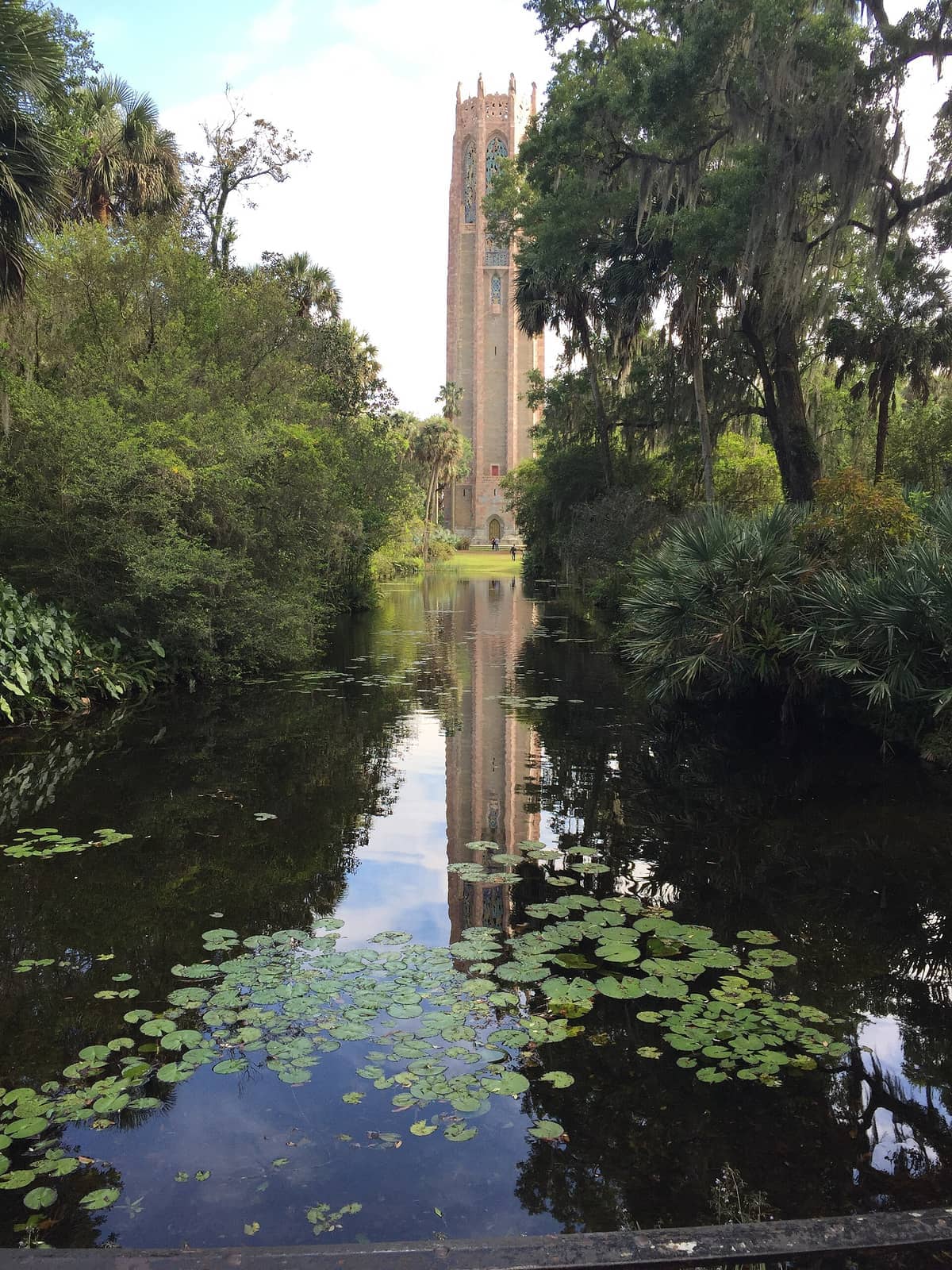 Der Glockenturm der Bok Tower Gardens spiegelt sich in einem ruhigen Seerosenteich, umgeben von üppigen grünen Bäumen und lebhafter Florida-Vegetation.