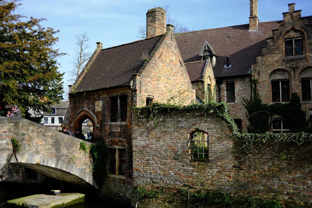 View of Bonifaciusbrug (Boniface Bridge) in Bruges, with its iconic stone arch and historic brick buildings behind, surrounded by greenery.
