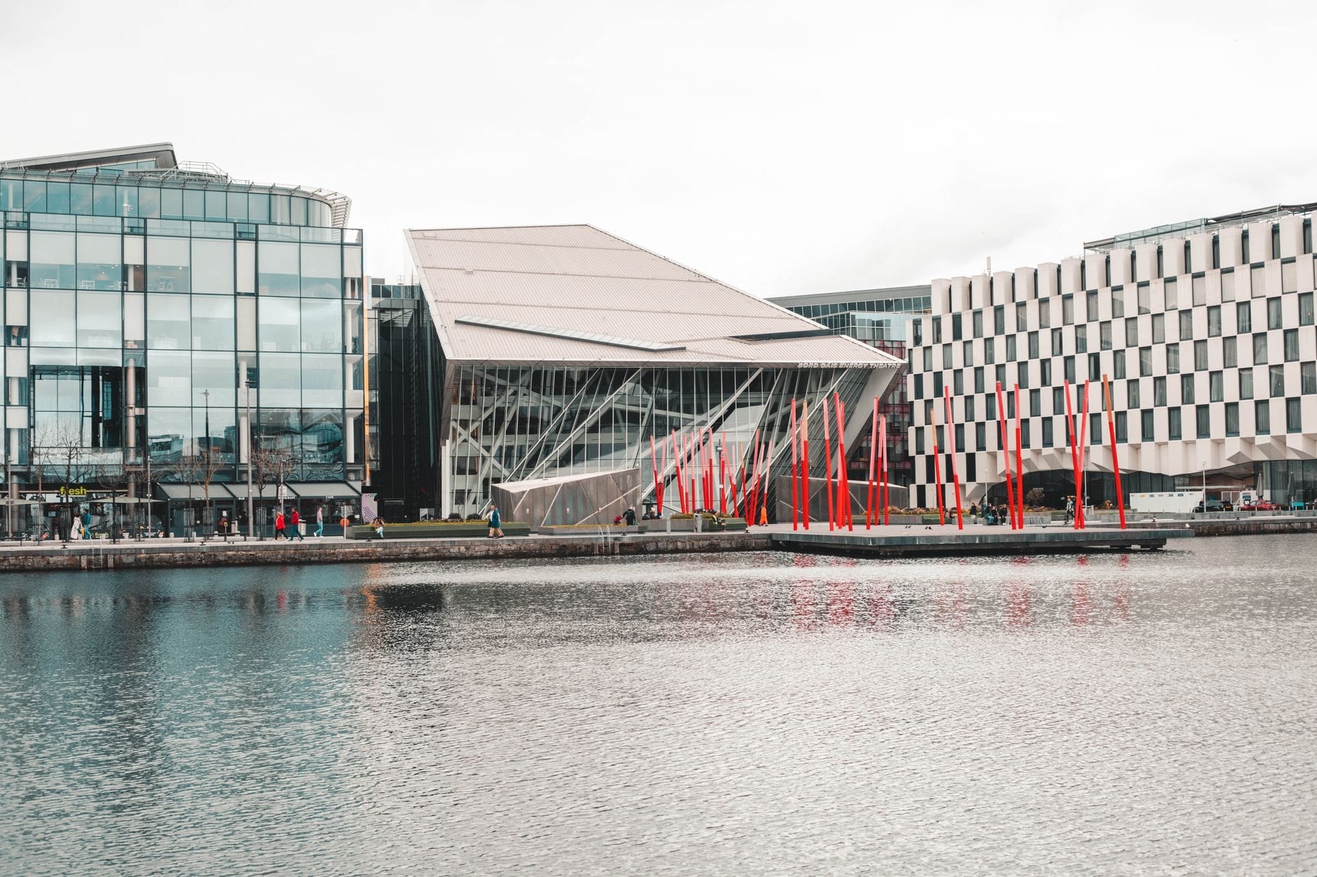 Vista esterna del Bord Gáis Energy Theatre a Dublino, con la sua architettura moderna, il caratteristico tetto inclinato, l'acqua circostante e i vivaci pali rossi di Grand Canal Square.