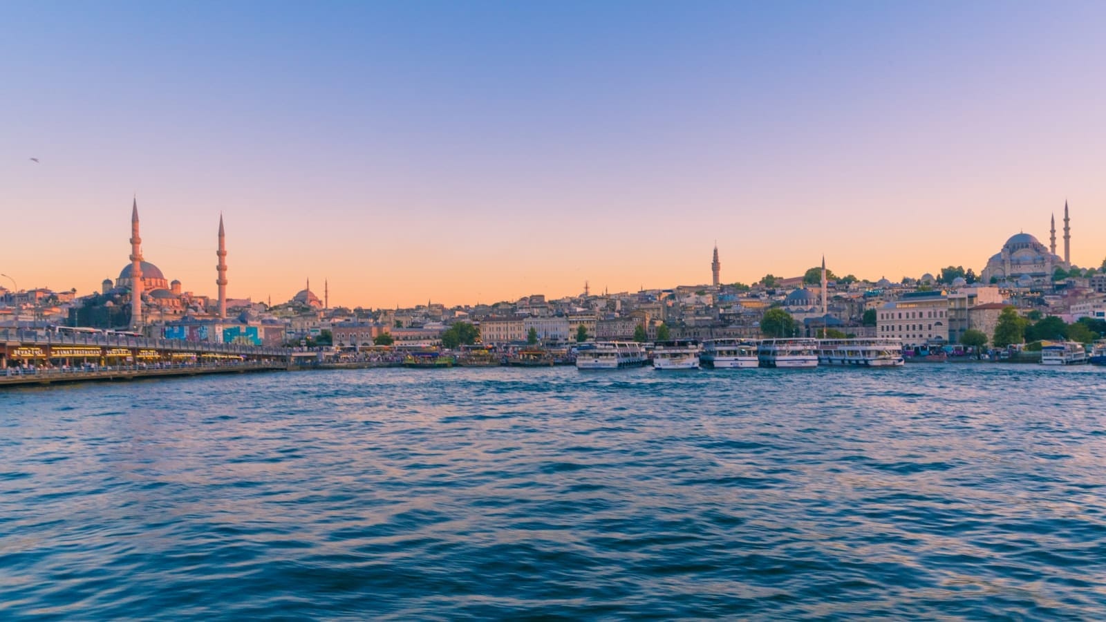 Vista panorâmica do horizonte de Istambul ao pôr do sol, mesquitas com minaretes, céu colorido, várias balsas e barcos cruzando o Bósforo e prédios da cidade ao longo da orla.
