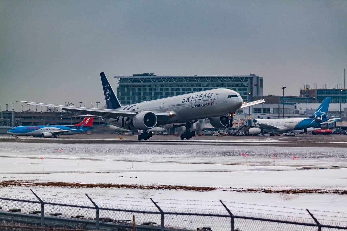 Verschneite Flughafenpiste mit einem landenden Air France-Flugzeug und Terminals im Hintergrund, Winterwetter sichtbar.