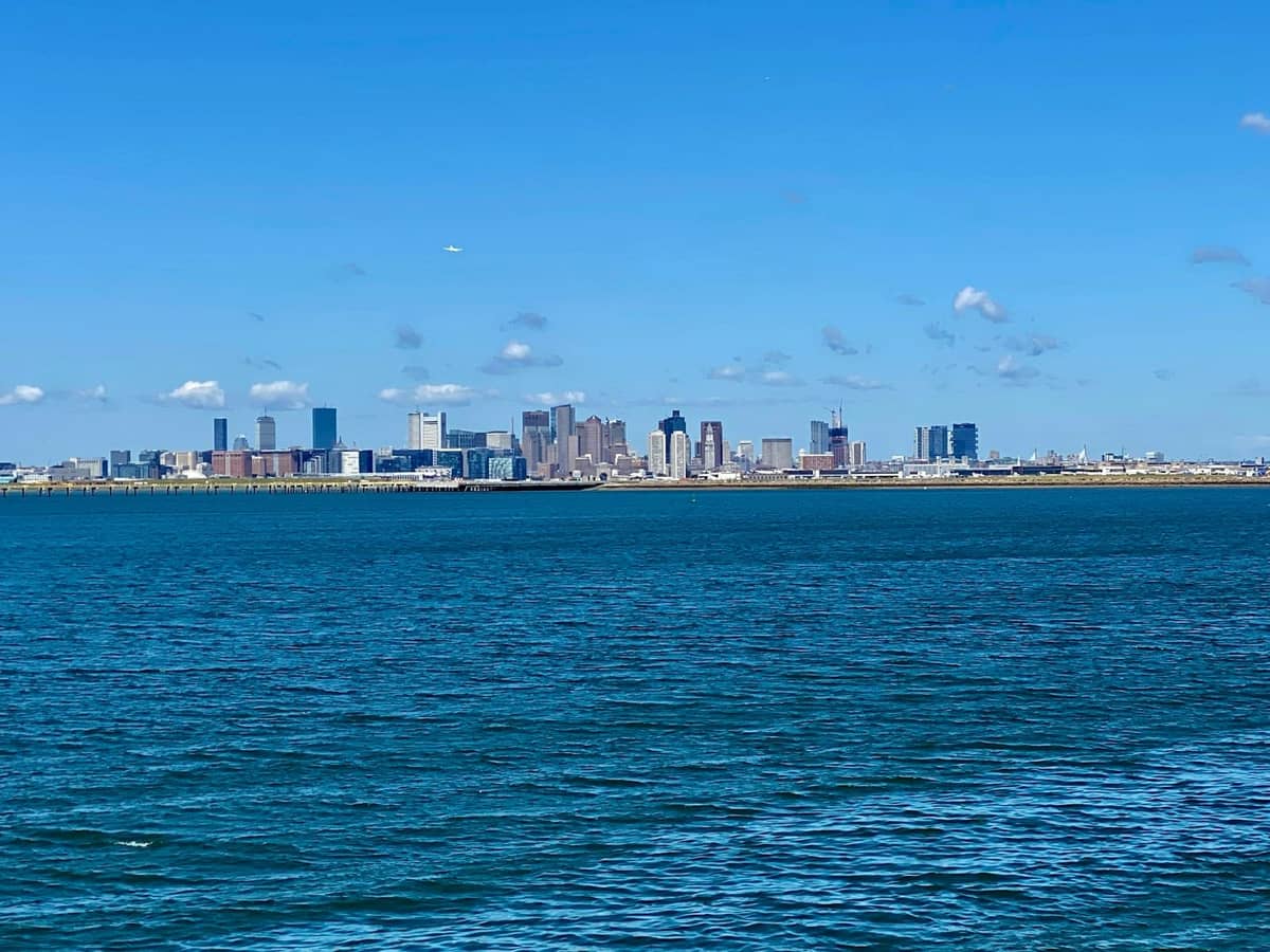 Weitläufiger Blick auf die Skyline von Boston über das blaue Wasser, von den Hafeninseln unter einem klaren Himmel aus gesehen.