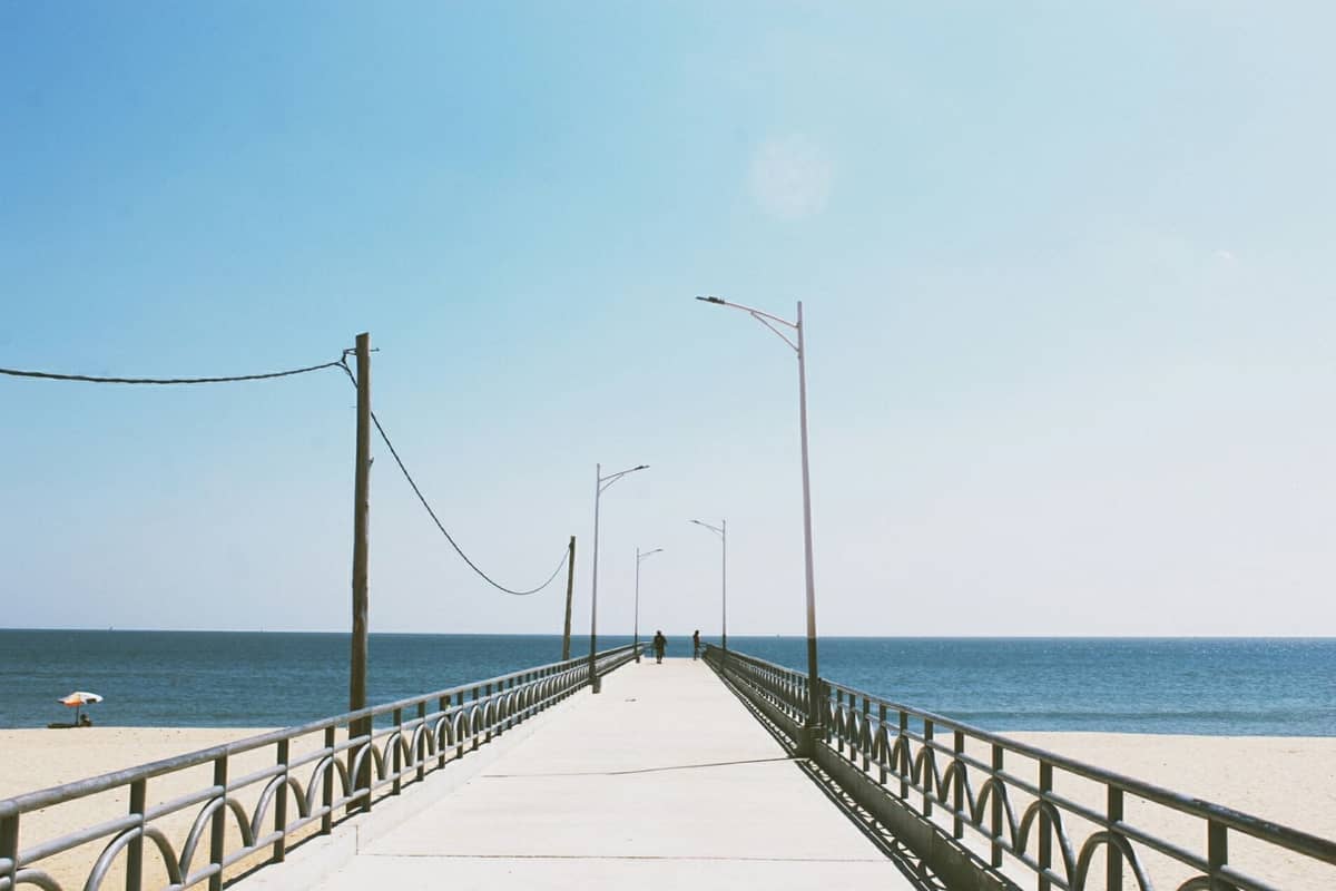 Ein breiter Pier, der sich in den Ozean erstreckt, mit Sand und ruhigem blauem Wasser, aufgenommen an einem sonnigen, klaren Tag.