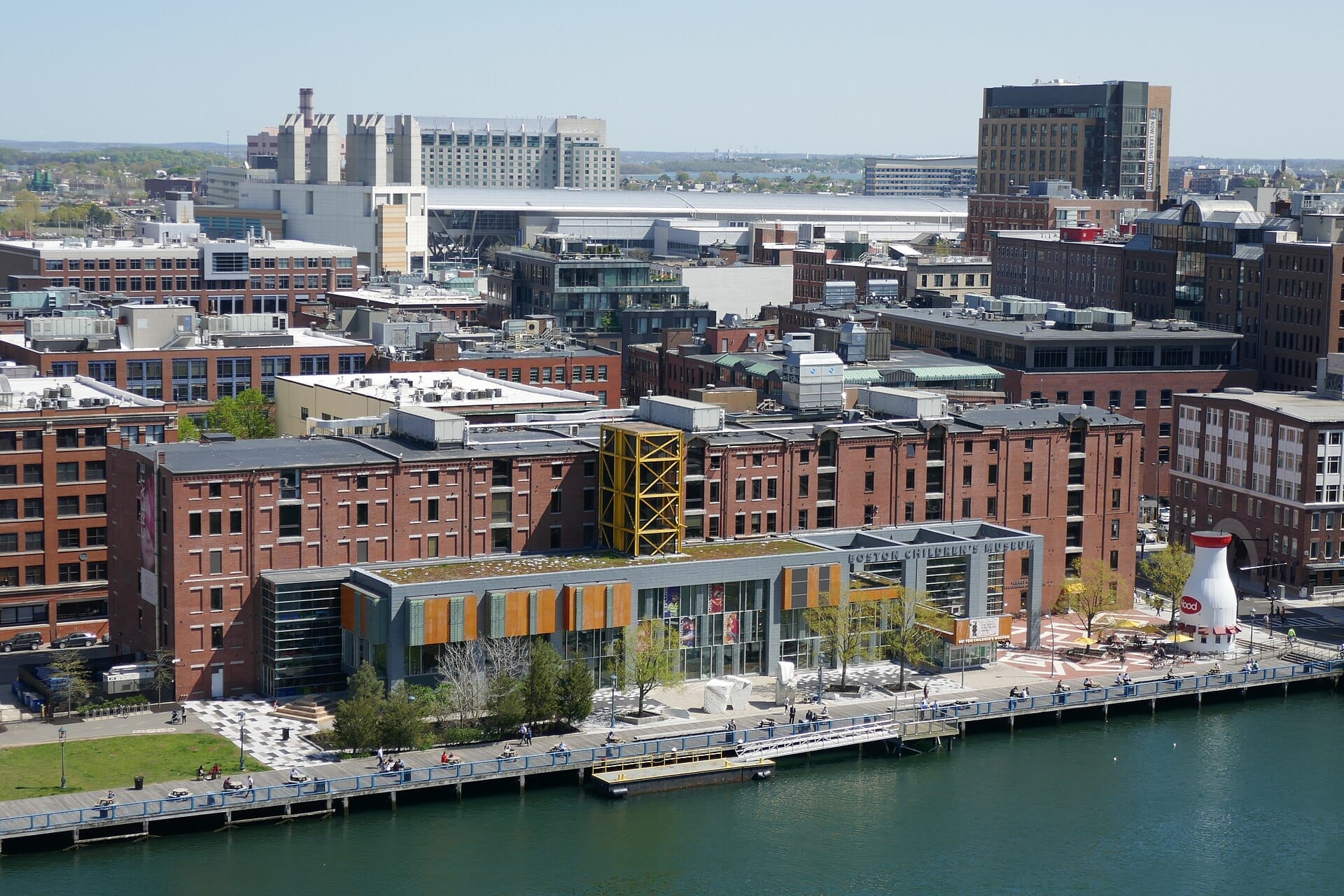 Vista aerea del Boston Children's Museum con il suo moderno ingresso in vetro, edifici in mattoni rossi, passerella e il canale Fort Point Channel in piena luce del giorno.
