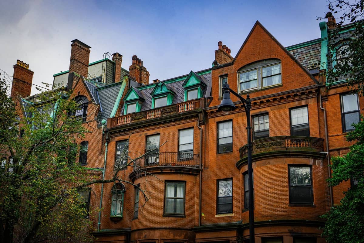 Casas adosadas de ladrillo con miradores y cornisas ornamentadas en el histórico barrio de Back Bay en Boston, enmarcadas por árboles y una farola.