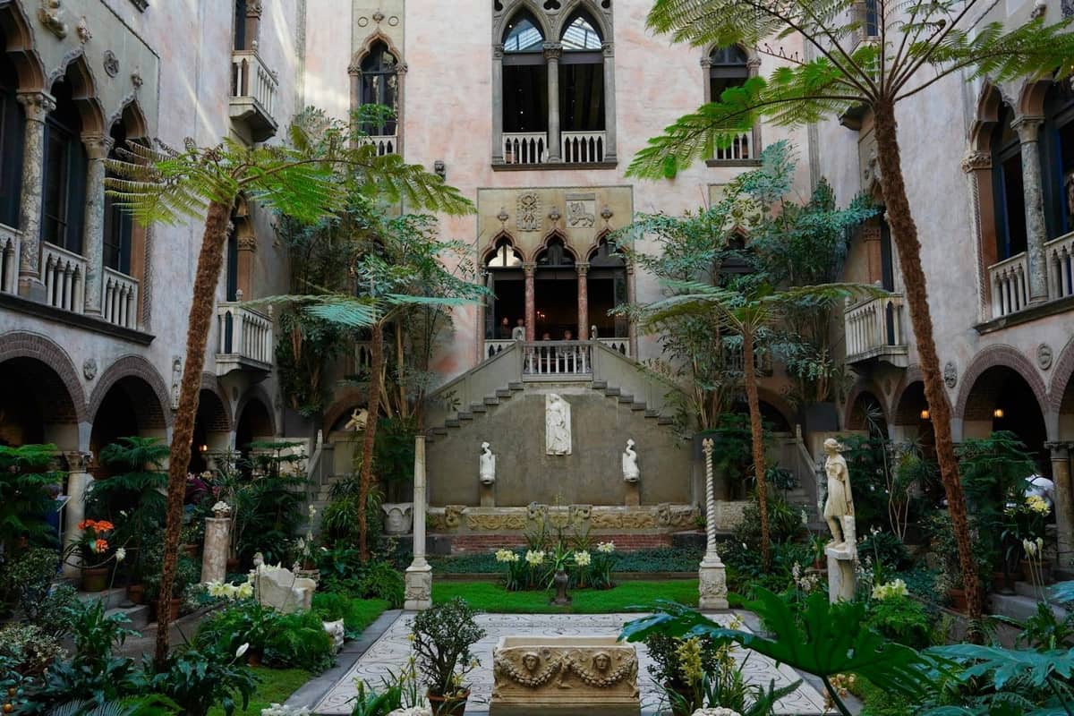 Vista amplia de un patio interior ornamentado con ventanas arqueadas, esculturas y exuberantes plantas en un histórico museo de Boston.