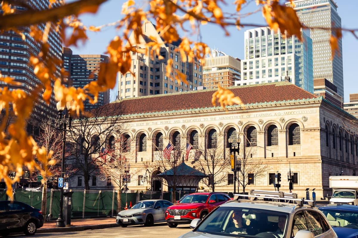 Boston Public Library an einem Herbsttag mit gelben Blättern im Vordergrund und Stadtgebäuden im Hintergrund.