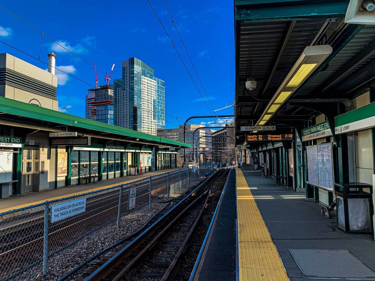 Blick auf eine oberirdische MBTA Green Line-Station in Boston, mit Stadtgebäuden im Hintergrund und deutlicher Beschilderung entlang des Bahnsteigs.