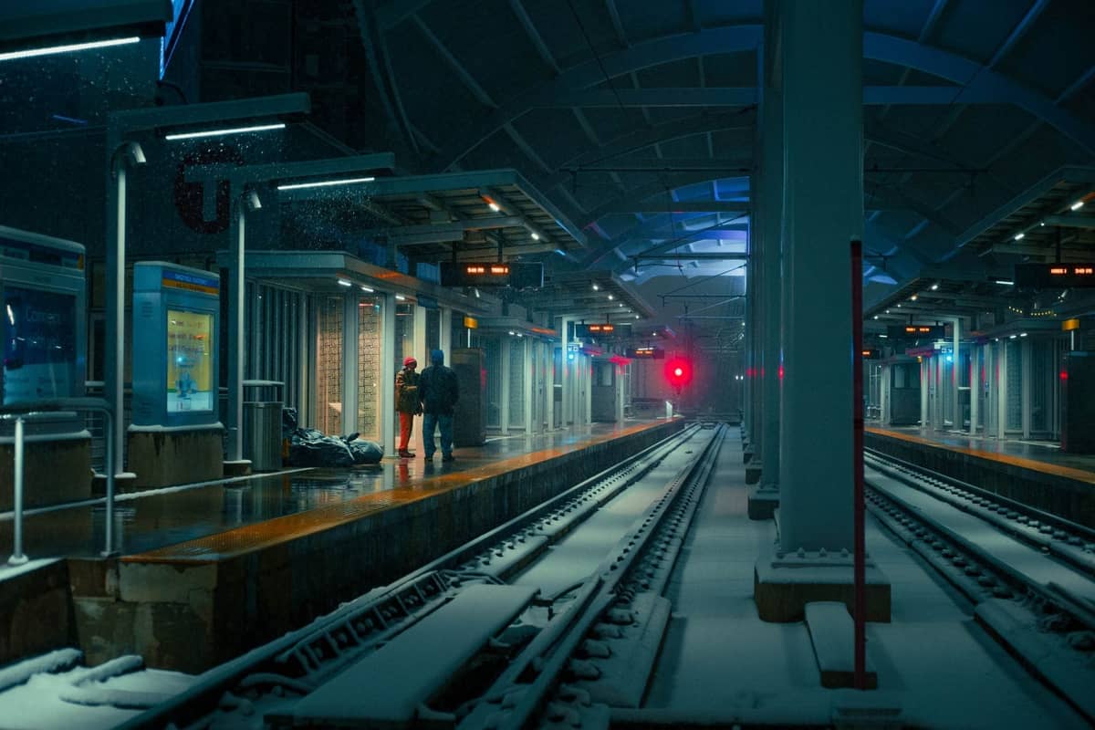 Andén de la estación de tránsito de Boston de noche con nieve en el suelo y personas esperando el tren.
