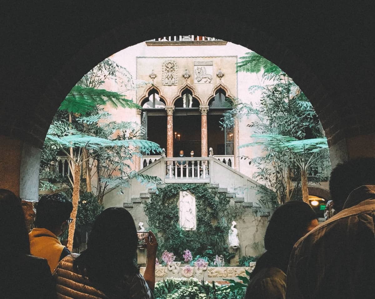 Visitantes se encuentran bajo un arco mirando hacia el jardín del patio del Isabella Stewart Gardner Museum en Boston.
