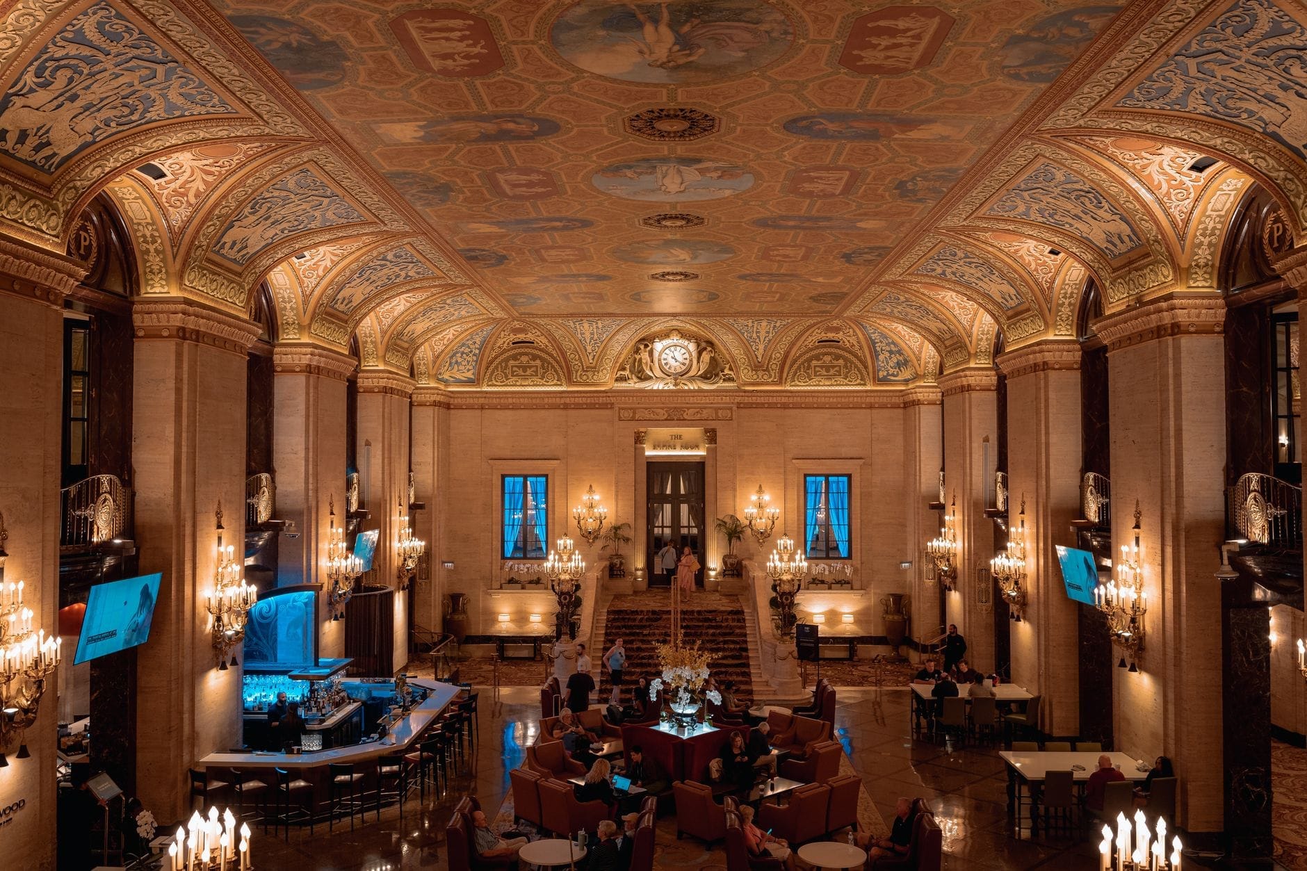 Saguão grandioso de hotel de luxo com tetos ornamentados, lustres e área de estar elegante, transmitindo opulência e sofisticação característica de Boston.