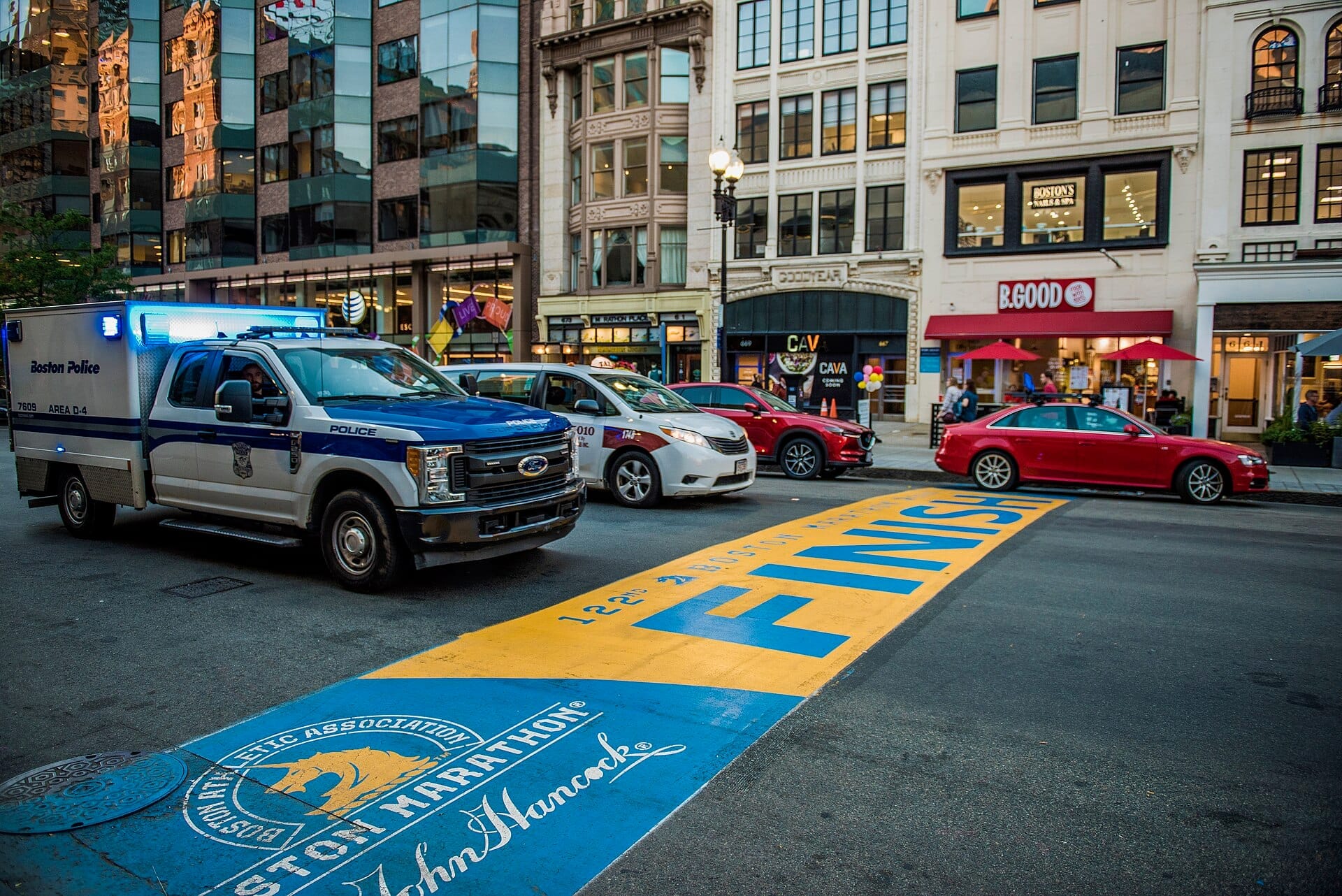 Linea del traguardo della Boston Marathon su Boylston Street, segnata in blu e giallo, con auto parcheggiate ed edifici vicini sullo sfondo.