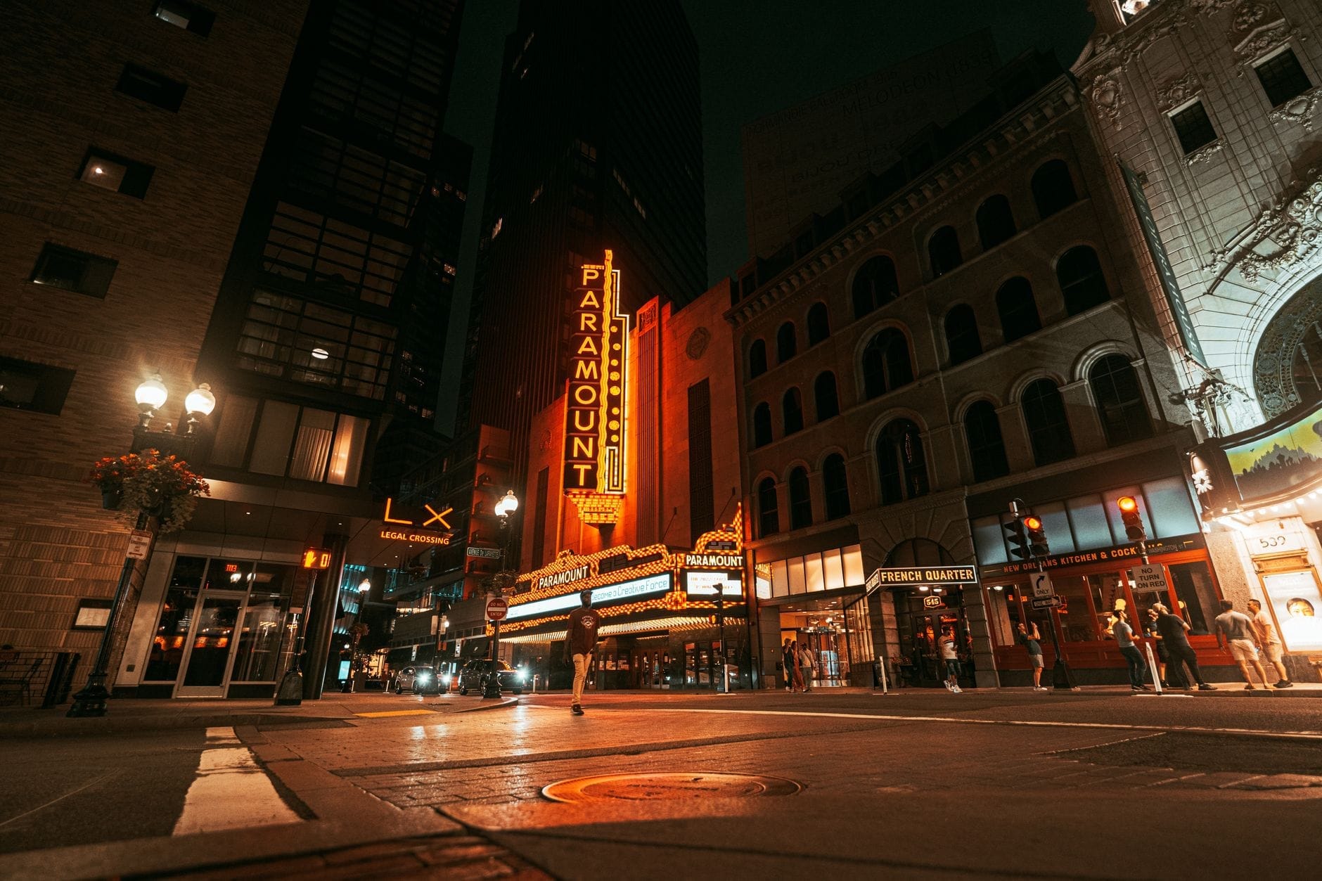 Centro de Boston à noite com letreiros de néon brilhantes, prédios históricos e pessoas caminhando em frente ao Paramount Theatre, transmitindo toda a energia da cidade após o anoitecer.