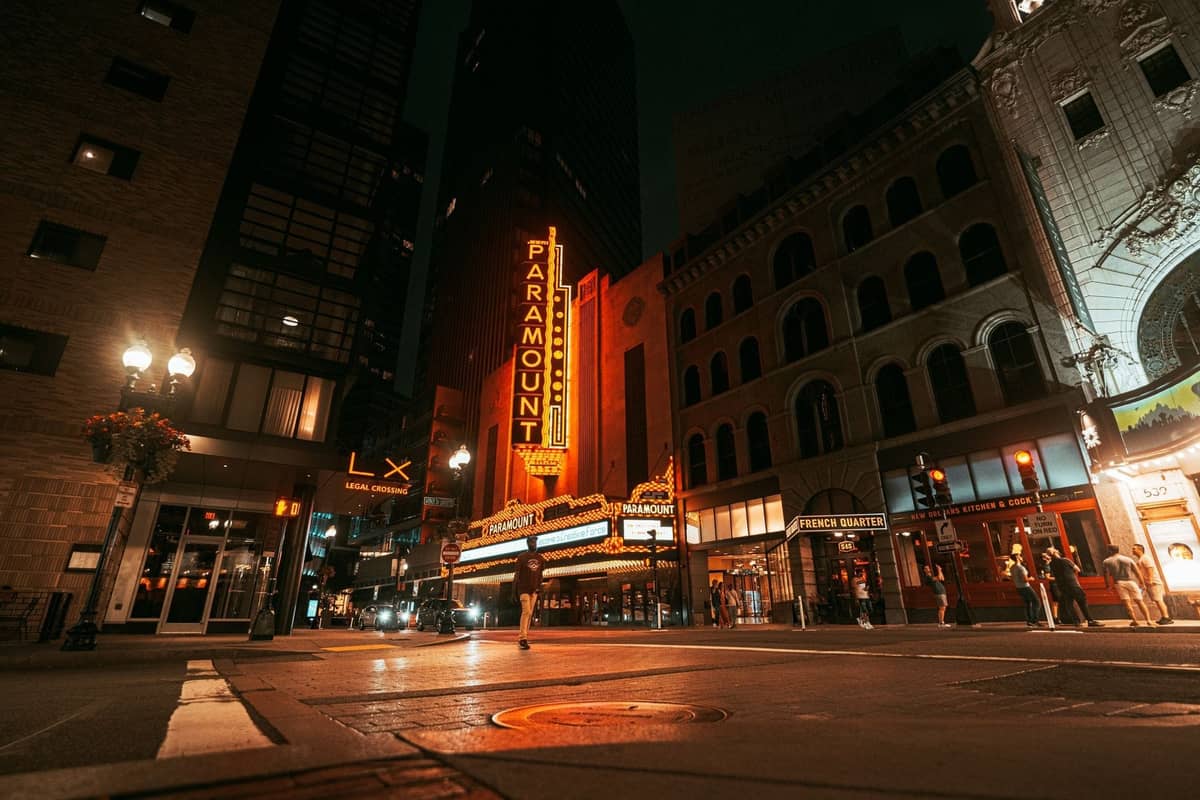 Vista della strada del Theater District di Boston di notte con l'insegna luminosa del Paramount accesa e persone che camminano davanti a club e bar illuminati.