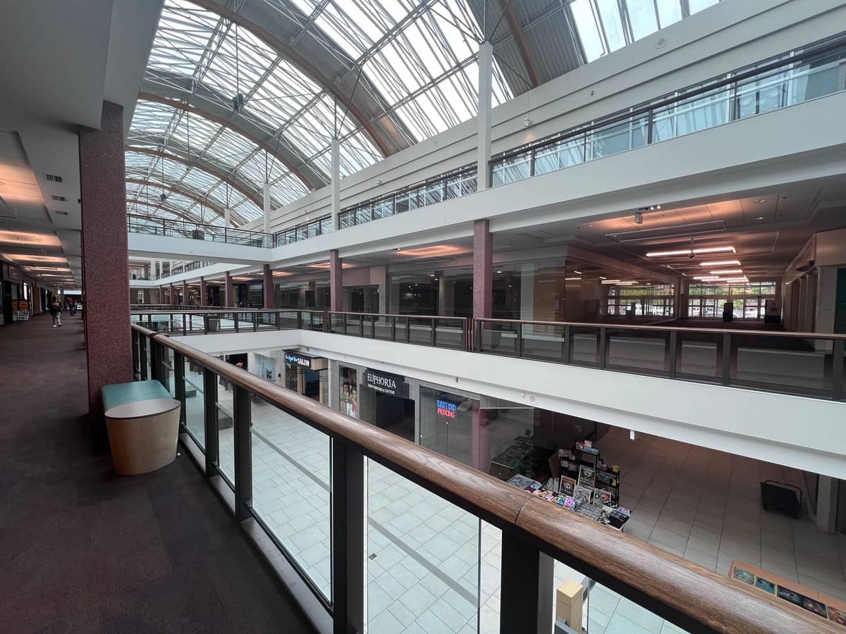 Intérieur lumineux d'un centre commercial avec plusieurs étages, plafond en verre, diverses enseignes et larges allées.