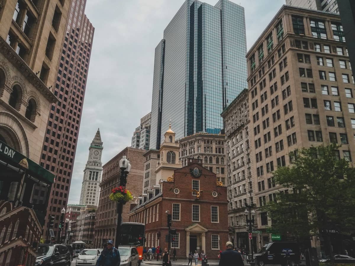 View of Boston's Old State House, a historic red-brick building, surrounded by modern skyscrapers and people walking on the street.