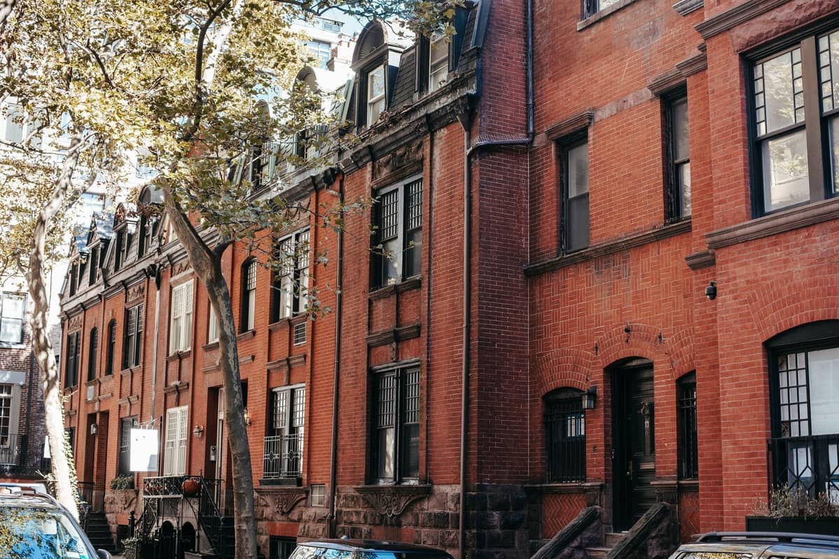 Rangée de maisons de ville historiques en grès brun avec des arbres et des voitures garées le long d'une rue résidentielle de Boston.