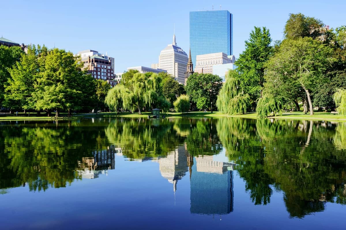 Boston Public Garden com o horizonte e salgueiros refletidos no lago em um dia ensolarado