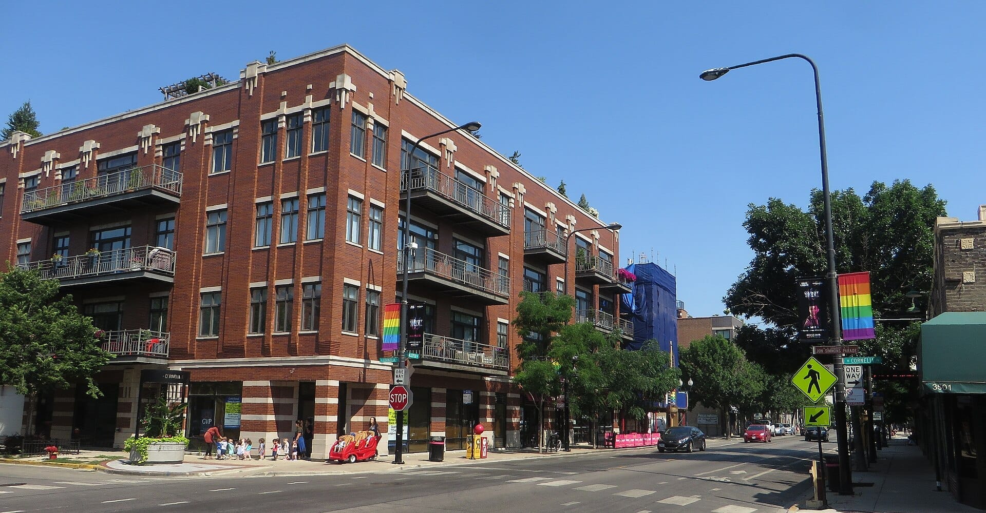 Edificio di appartamenti in mattoni rossi su North Halsted Street nel quartiere Boystown di Chicago, con bandiere arcobaleno del pride e pedoni sotto un cielo azzurro limpido.